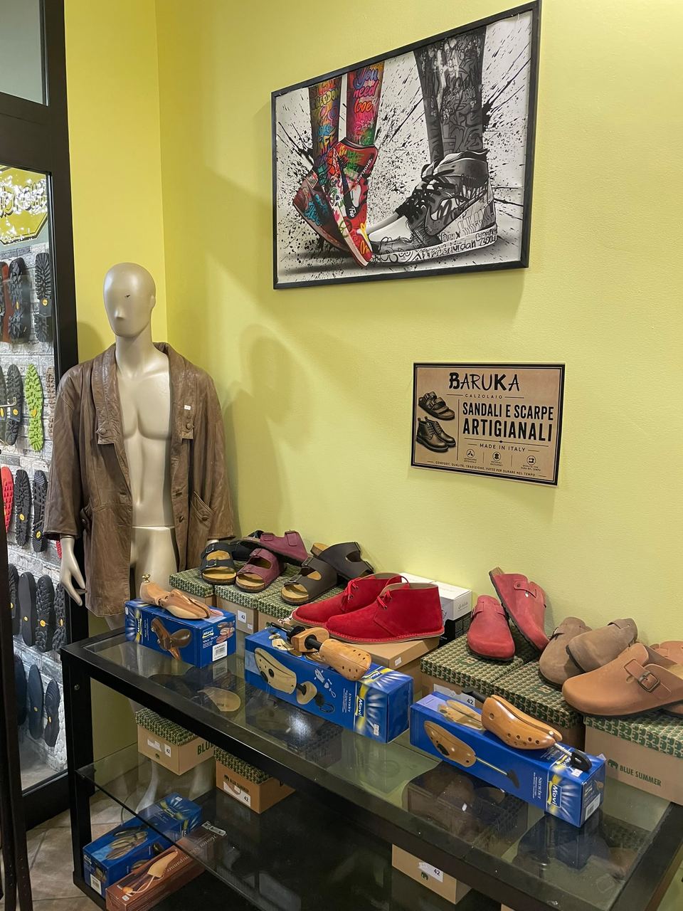 Sandali e scarpe esposti in bottega da Calzolaio Baruka, sotto il cartello "Sandali e scarpe artigianali"