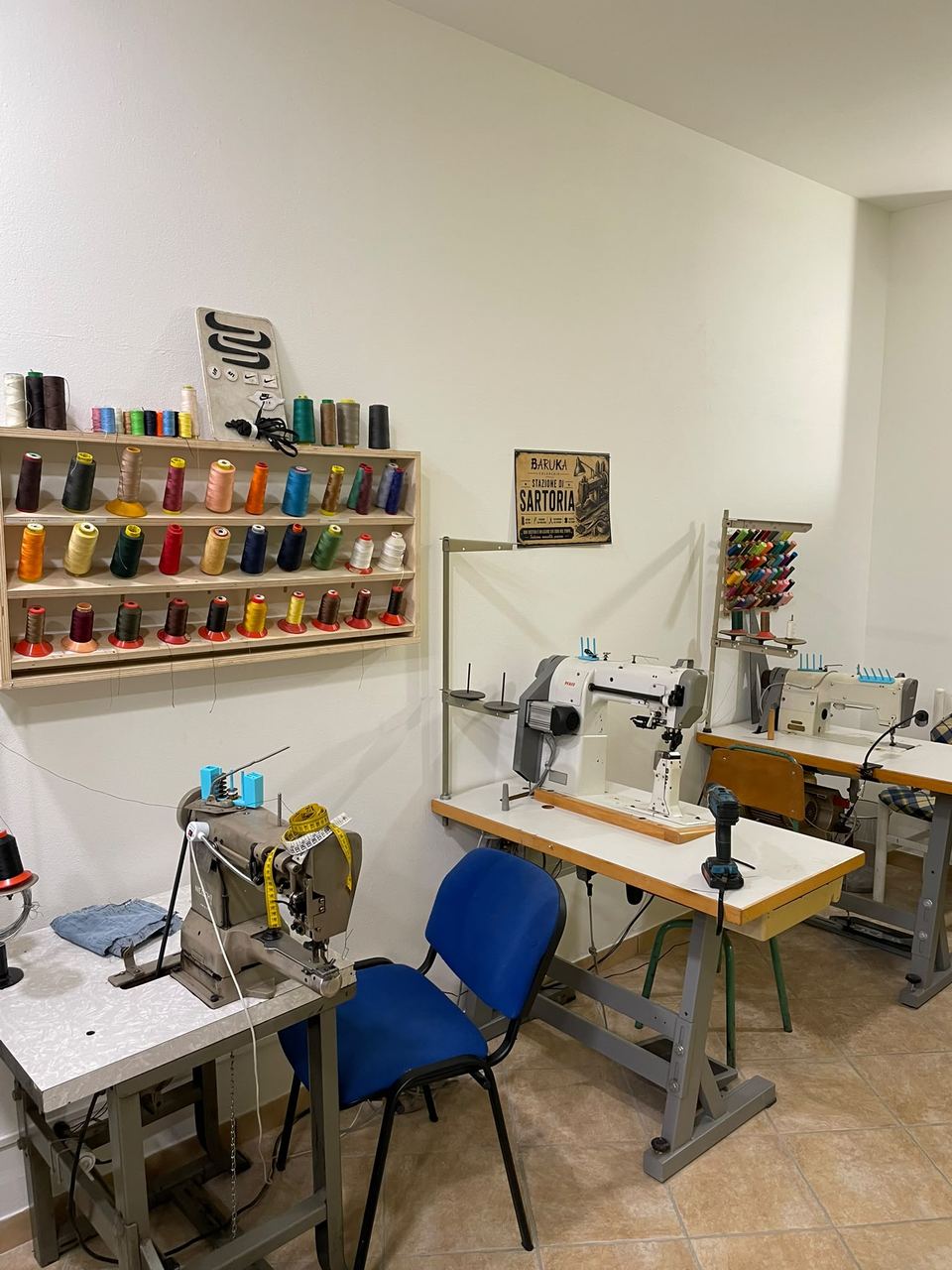 Il reparto sartoria di Calzolaio Baruka, con le macchine da cucire industriali e la rastrelliera dei fili