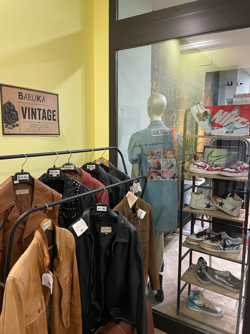 Giacche in pelle appese in bottega da Calzolaio Baruka, sotto il cartello "Vintage"